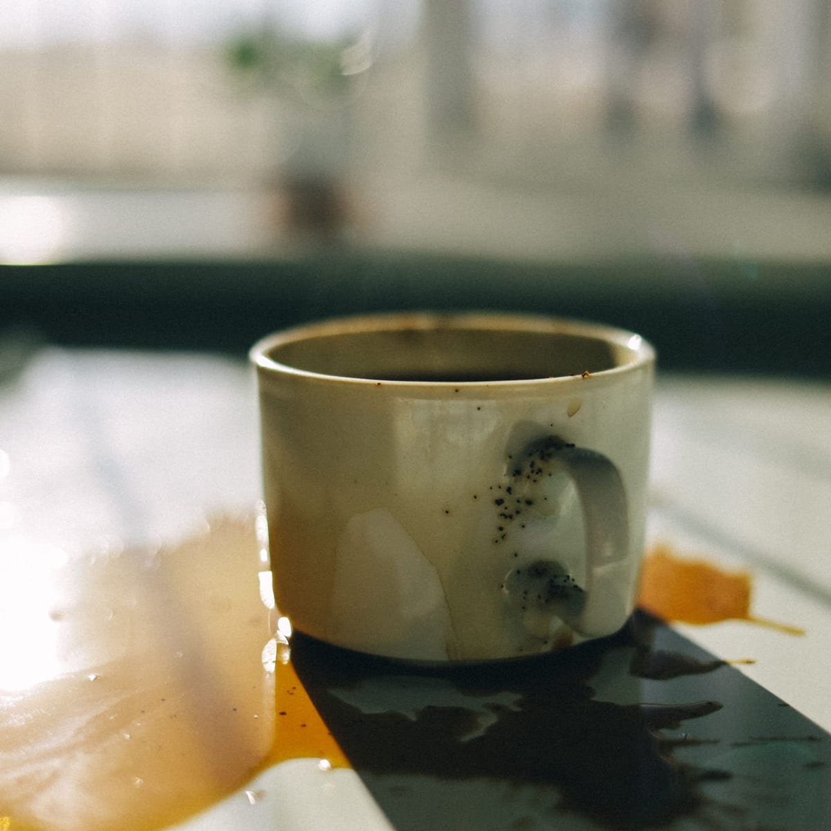 Kaffeebecher mit verschüttetem Kaffee auf einem Tisch am Fenster
