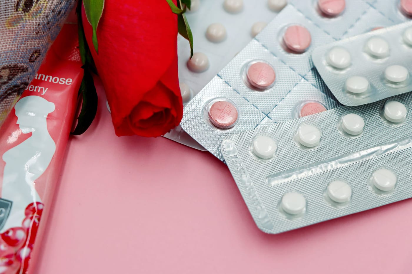 Pill packs next to a red rose on a pink surface