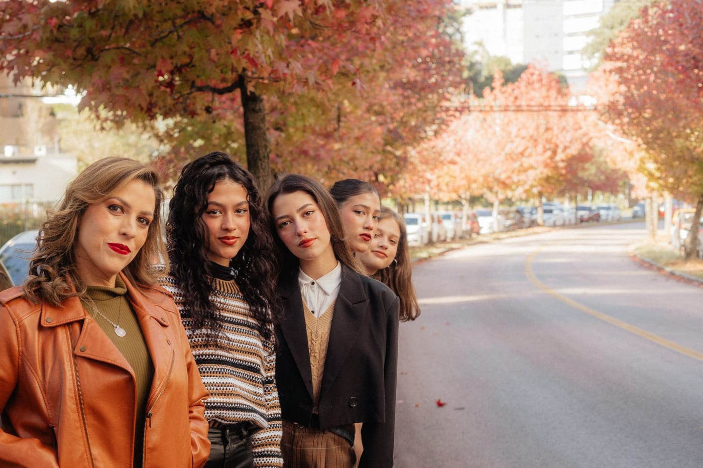 Four women standing together on a tree-lined street in autumn