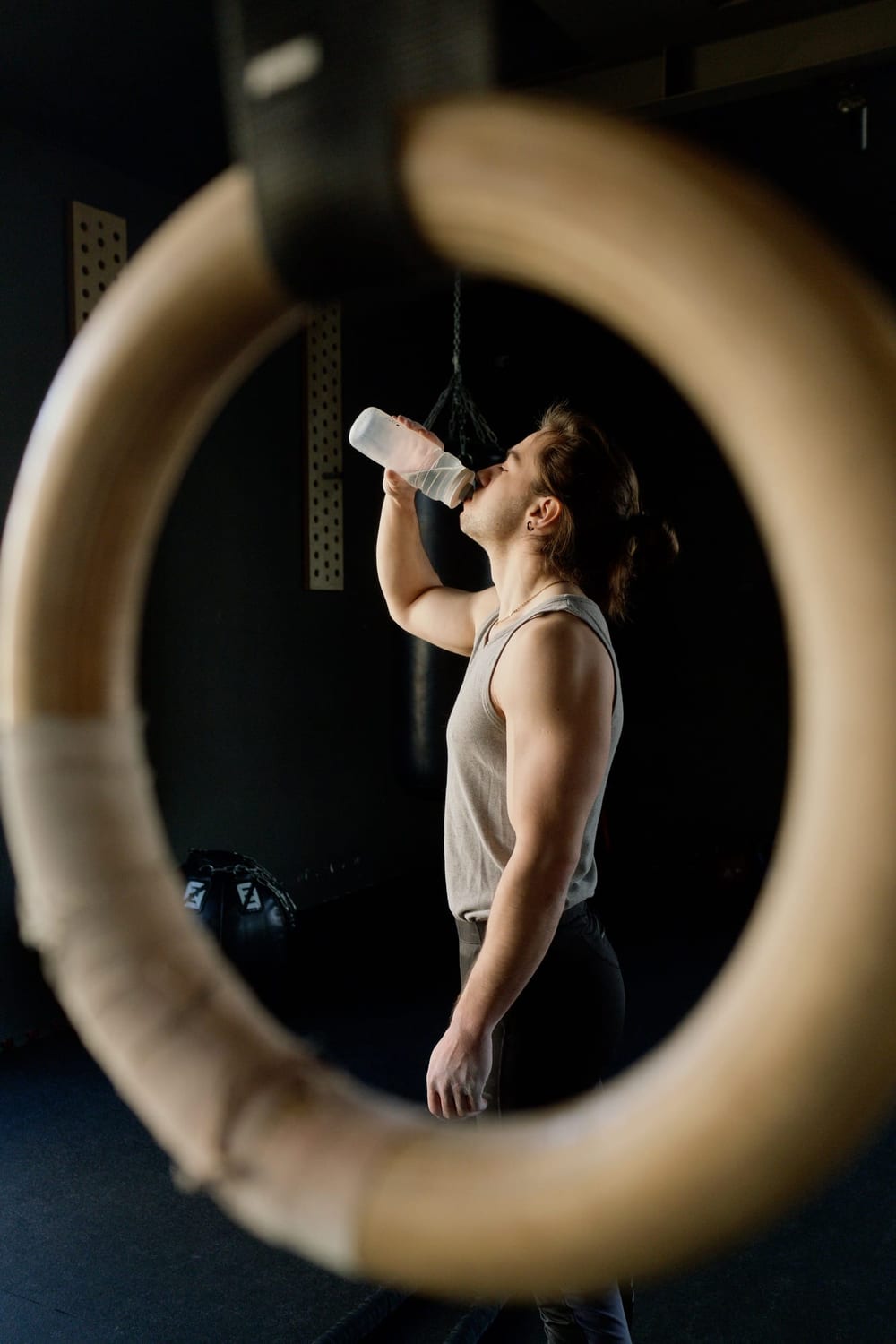 Athlete drinking from a water bottle framed by gymnastic rings