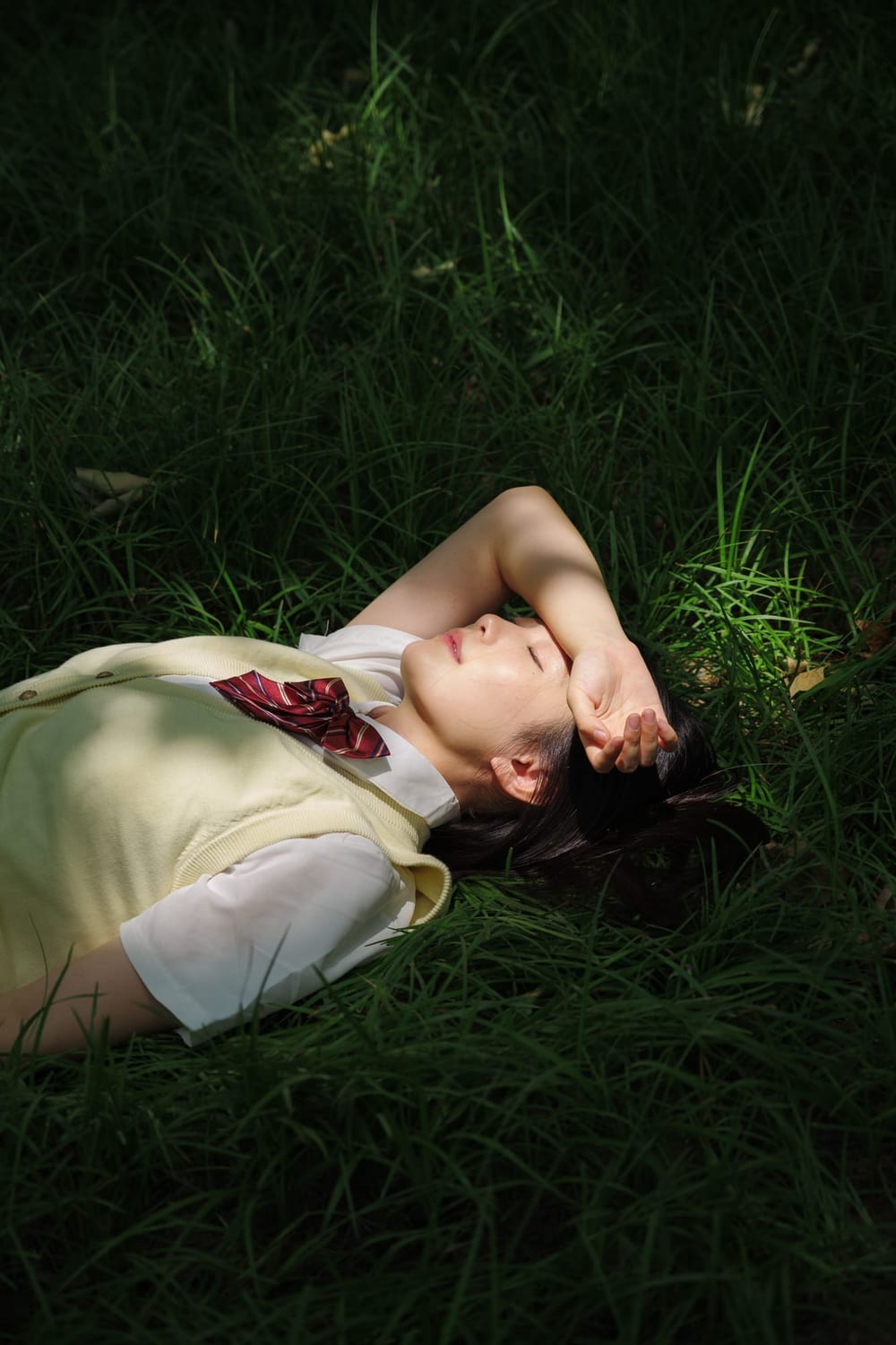 Woman lying on grass with her arm over her eyes