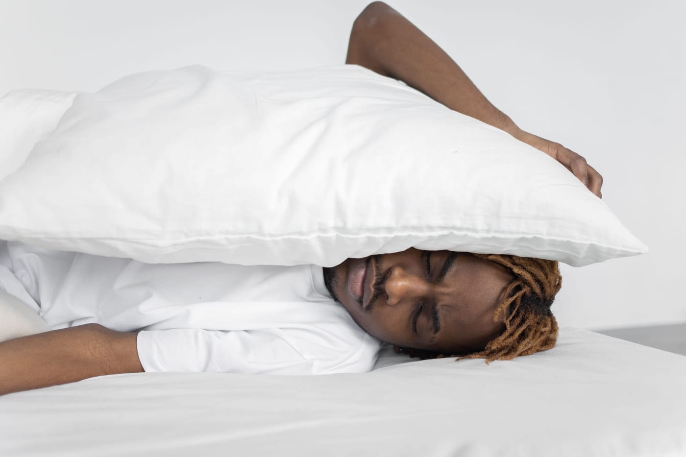 Man lying in bed with a pillow over his head