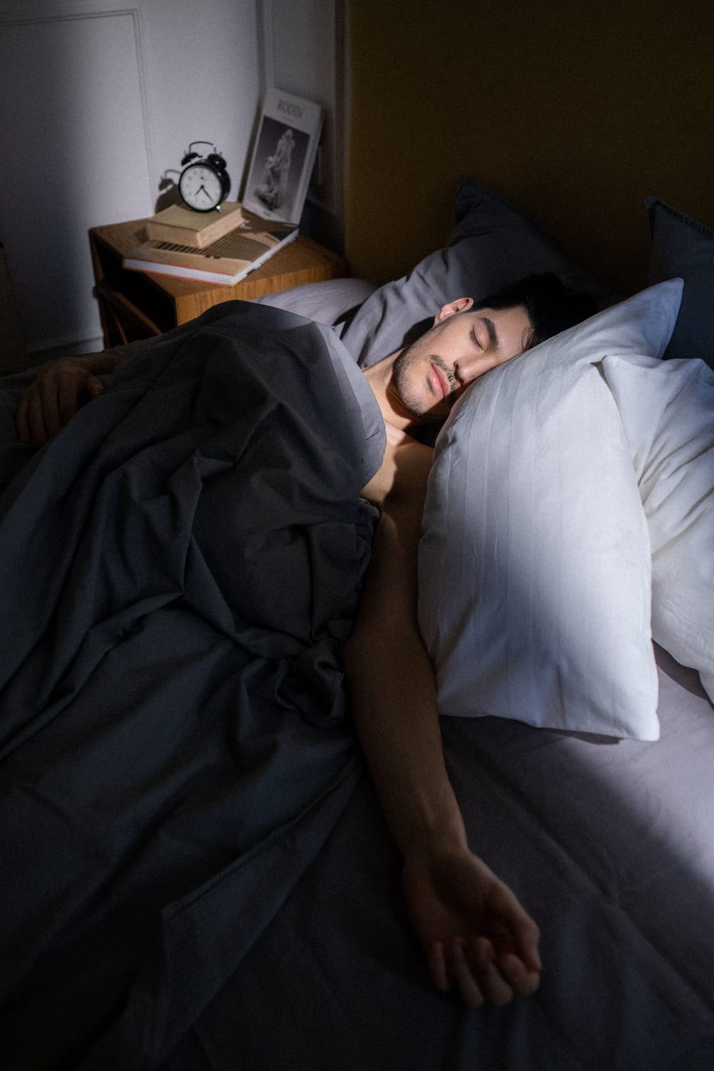Man asleep in bed with an alarm clock on the nightstand